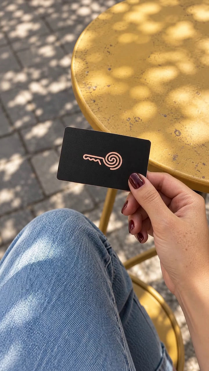 A hand holding a black MI8OS Card with a rose-gold key at a café